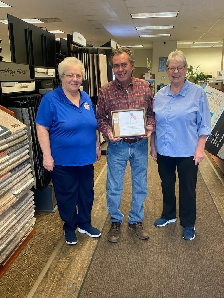 Jim and team holding a framed certificate in The Floor Store showroom surrounded by flooring samples