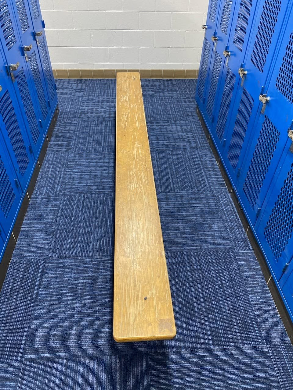 Blue patterned carpet tile installed in a locker room between rows of blue lockers with a wooden bench